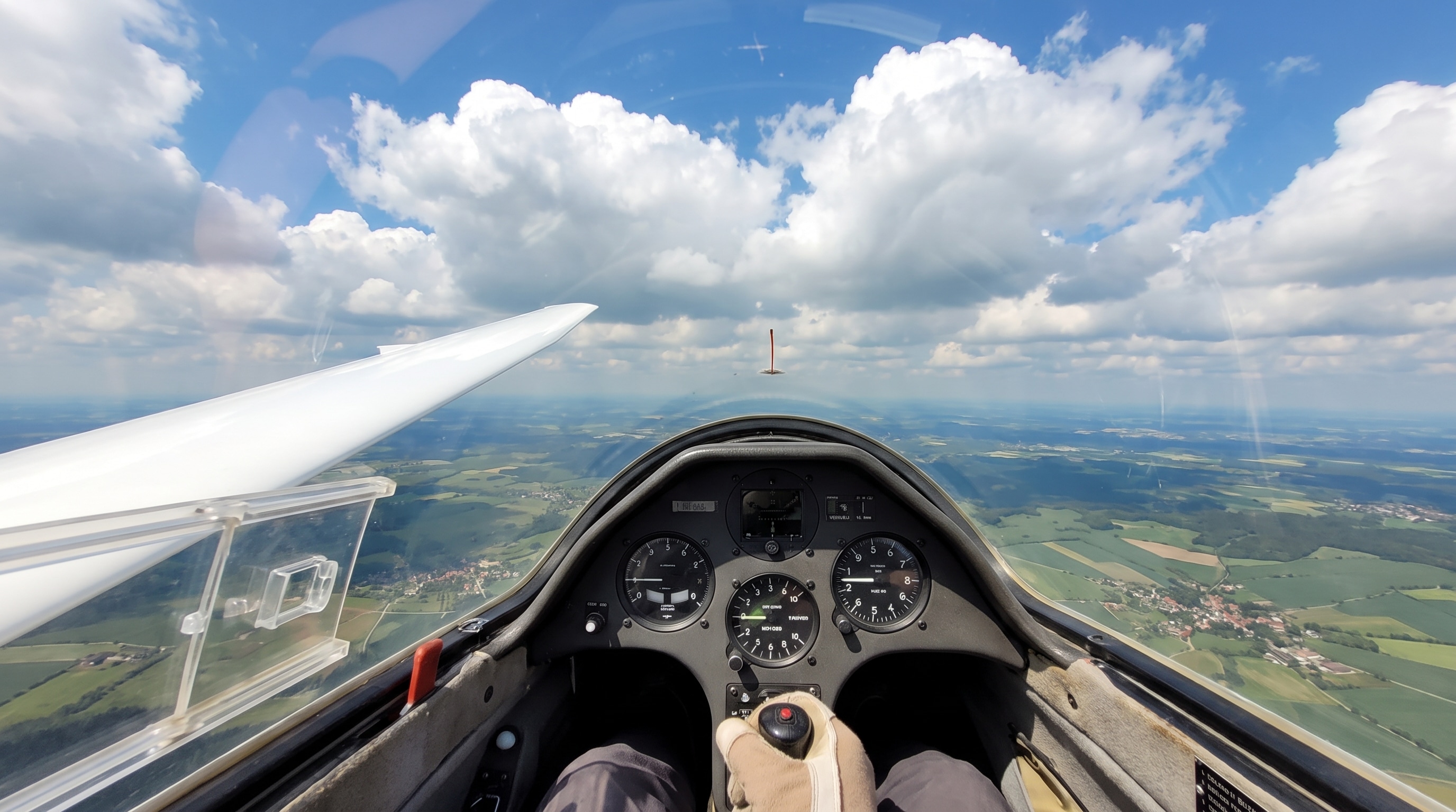Blick aus dem Cockpit eines Segelflugzeugs über die Instrumente und die lange weiße Fläche auf Wolken und Landschaft